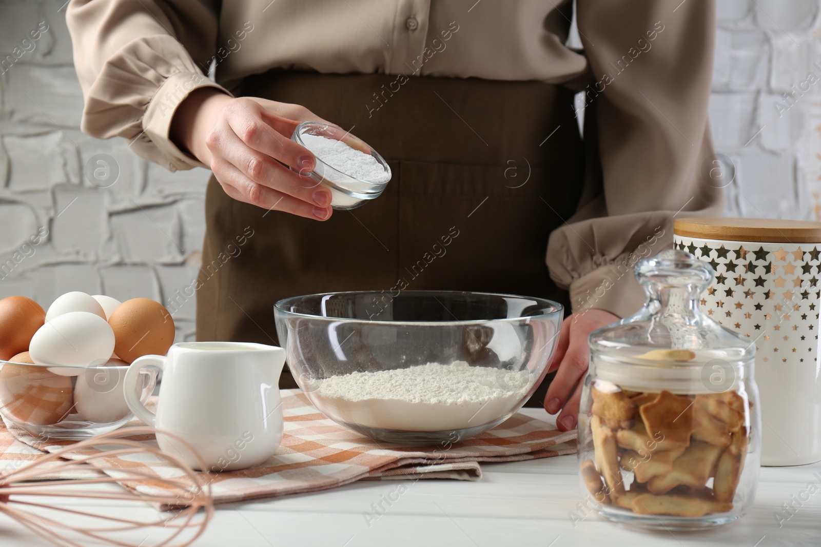 Photo of Woman adding baking powder into bowl at white wooden table, closeup