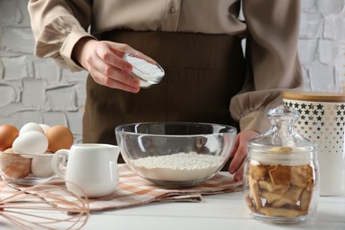 Photo of Woman adding baking powder into bowl at white wooden table, closeup