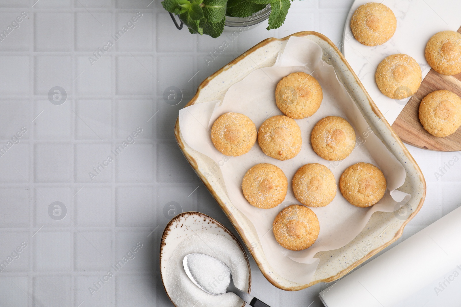 Photo of Tasty sweet sugar cookies in baking dish and mint on white tiled table, flat lay. Space for text