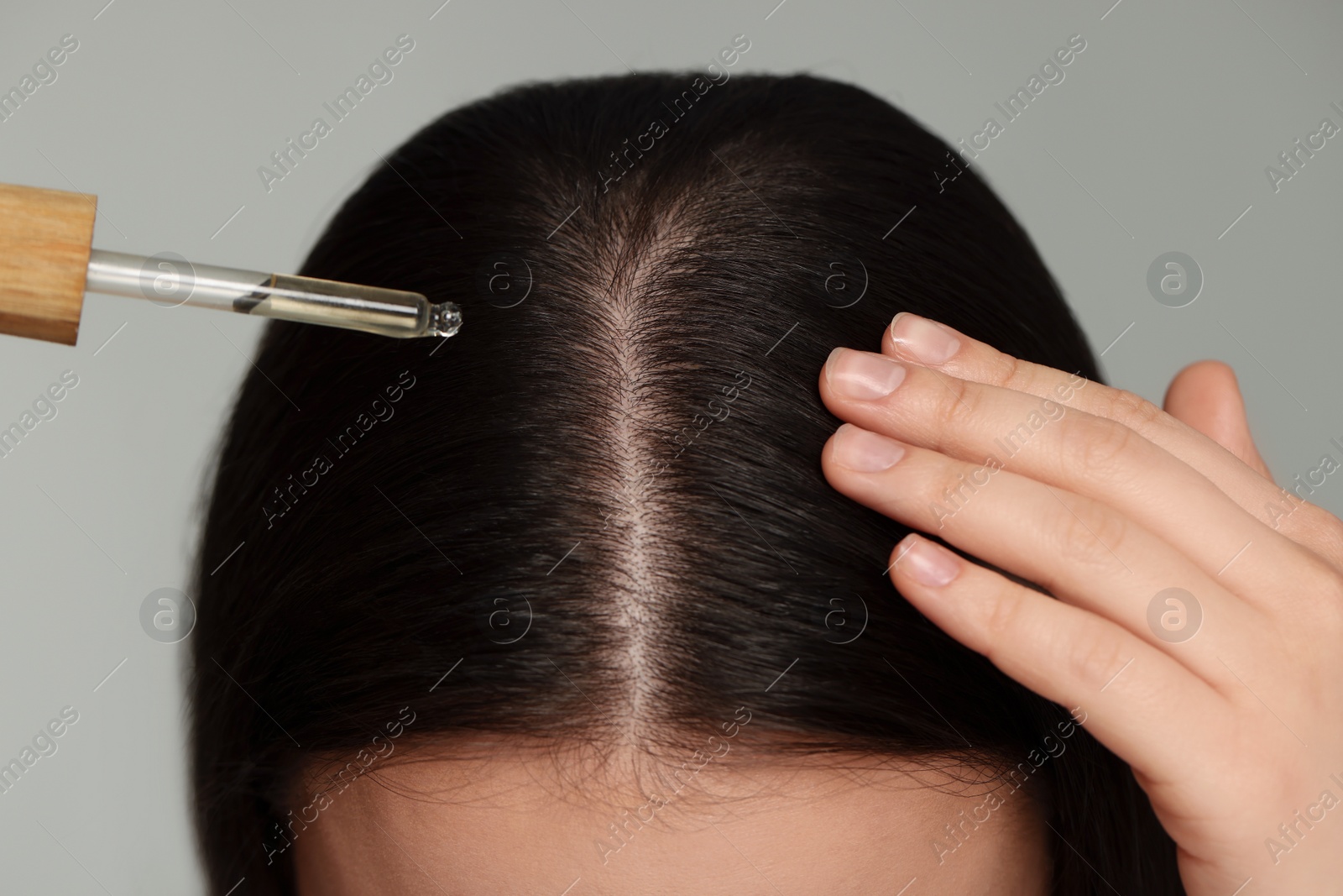 Photo of Woman applying essential oil onto hair on grey background, closeup