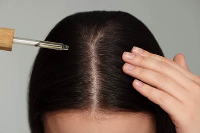 Photo of Woman applying essential oil onto hair on grey background, closeup