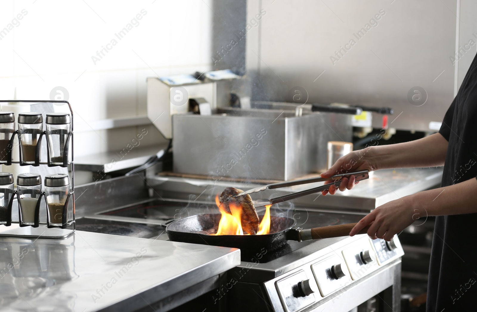 Photo of Female chef cooking meat with burning flame on stove in restaurant kitchen, closeup