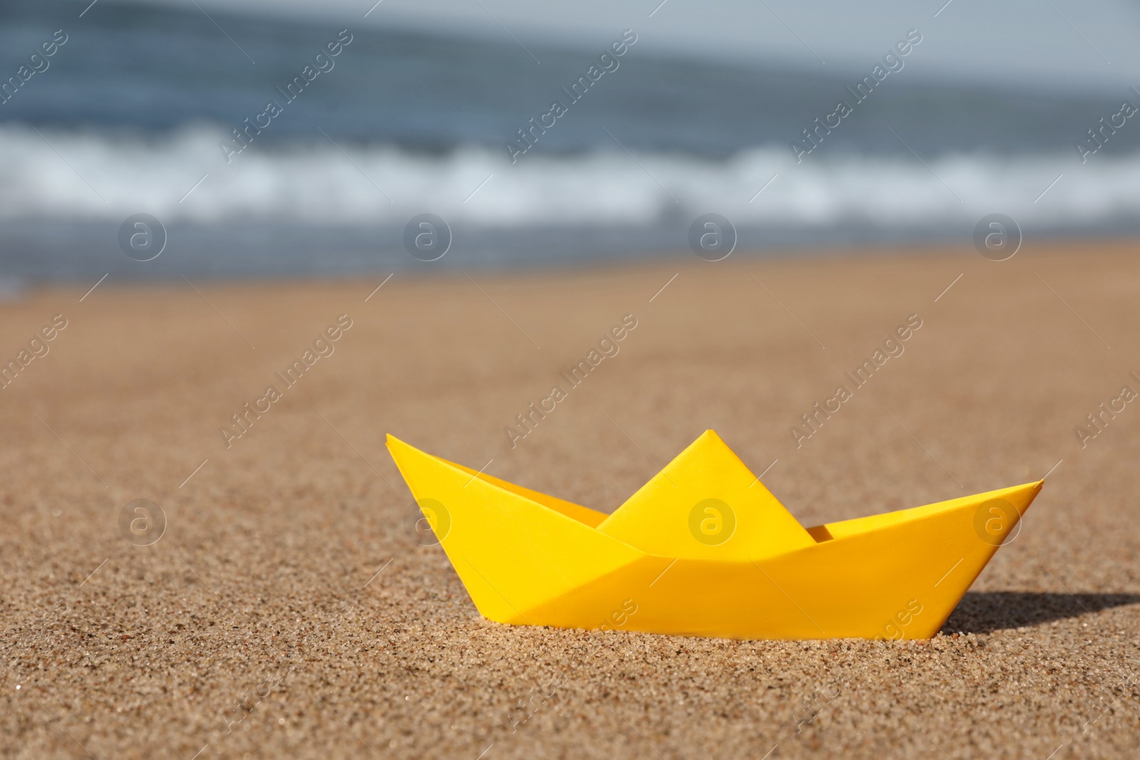 Photo of Yellow paper boat near sea on sandy beach, space for text