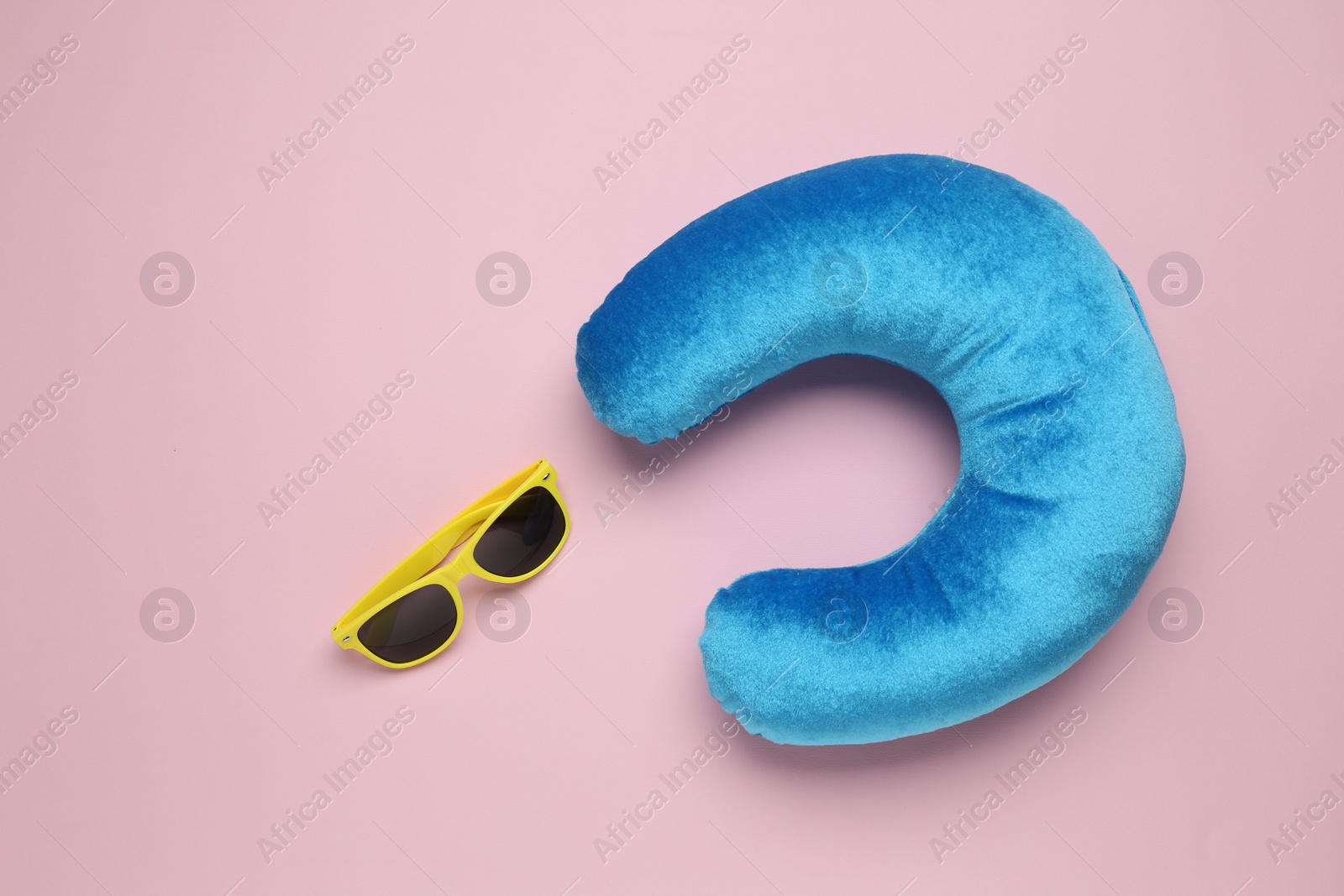 Photo of Light blue travel pillow and sunglasses on pink background, flat lay. Space for text