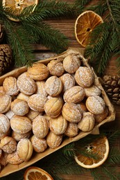 Photo of Delicious nut shaped cookies with boiled condensed milk, dry orange slices and fir tree branches on wooden table, flat lay