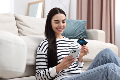 Happy young woman with credit card using smartphone for shopping online at home