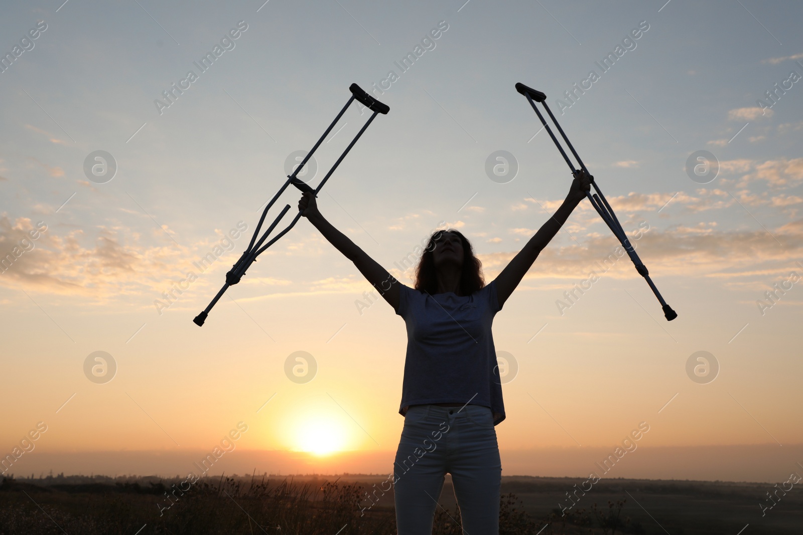 Photo of Woman holding axillary crutches outdoors at sunrise. Healing miracle