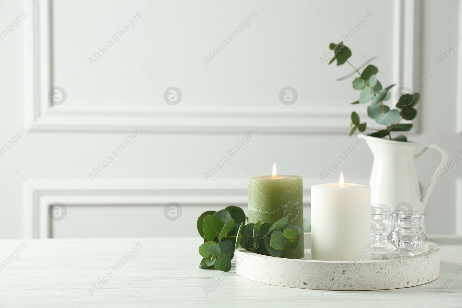 Photo of Burning candles and branches of eucalyptus on white table indoors, space for text