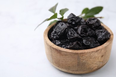 Sweet dried prunes in bowl on white table, closeup. Space for text