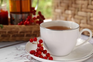Cup of hot drink and viburnum berries on white wooden table indoors, closeup