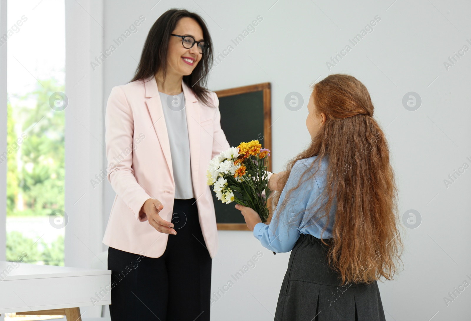 Photo of Schoolgirl with bouquet congratulating her pedagogue in classroom. Teacher's day