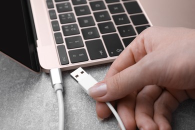 Photo of Woman holding plugged USB cable into laptop at grey table, closeup