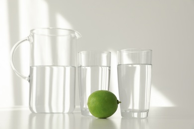 Glassware of fresh water and lime on table against light background