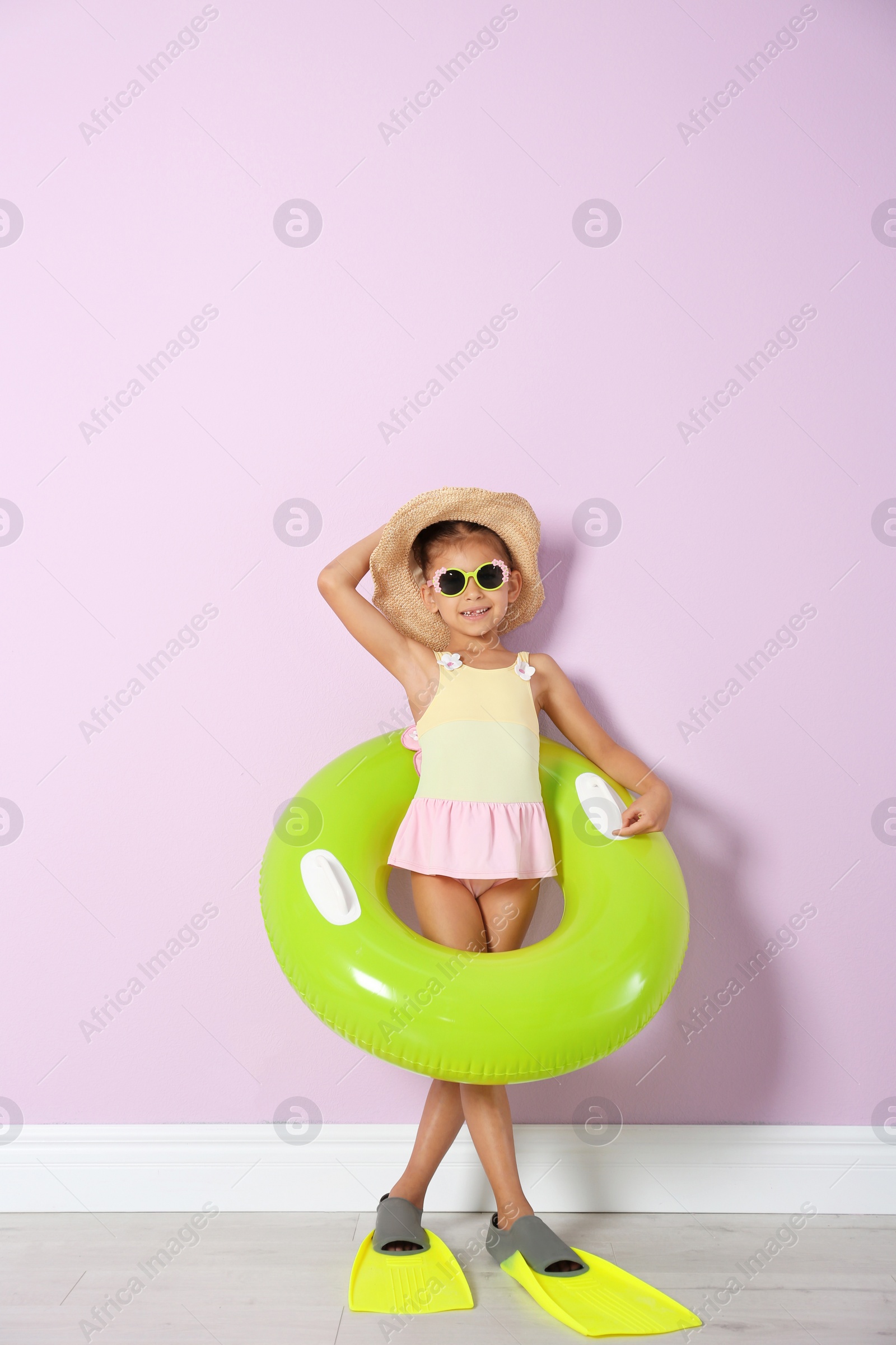 Photo of Cute little girl with inflatable ring wearing flippers near color wall