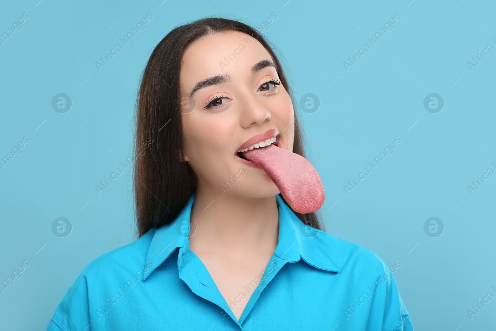 Image of Portrait of beautiful woman showing long tongue on light blue background