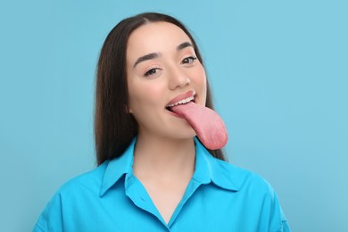 Portrait of beautiful woman showing long tongue on light blue background