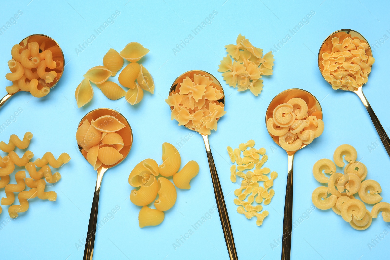 Photo of Spoons with different types of pasta on light blue background, flat lay