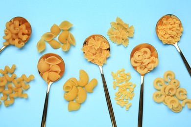 Spoons with different types of pasta on light blue background, flat lay