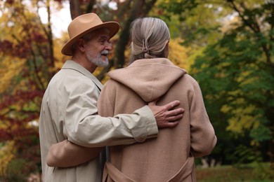 Photo of Affectionate senior couple walking in autumn park, back view