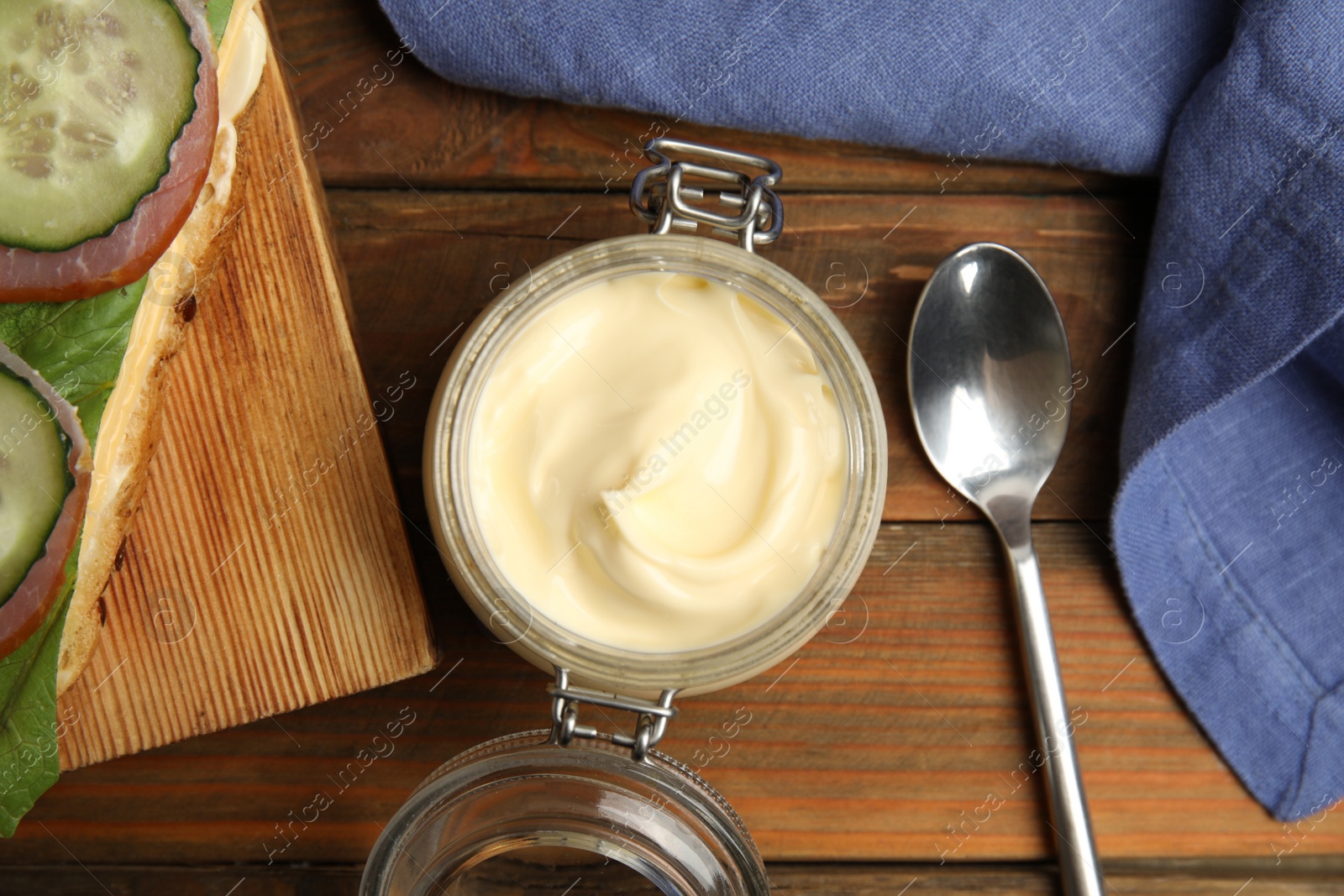 Photo of Jar of delicious mayonnaise near fresh sandwich on wooden table, flat lay