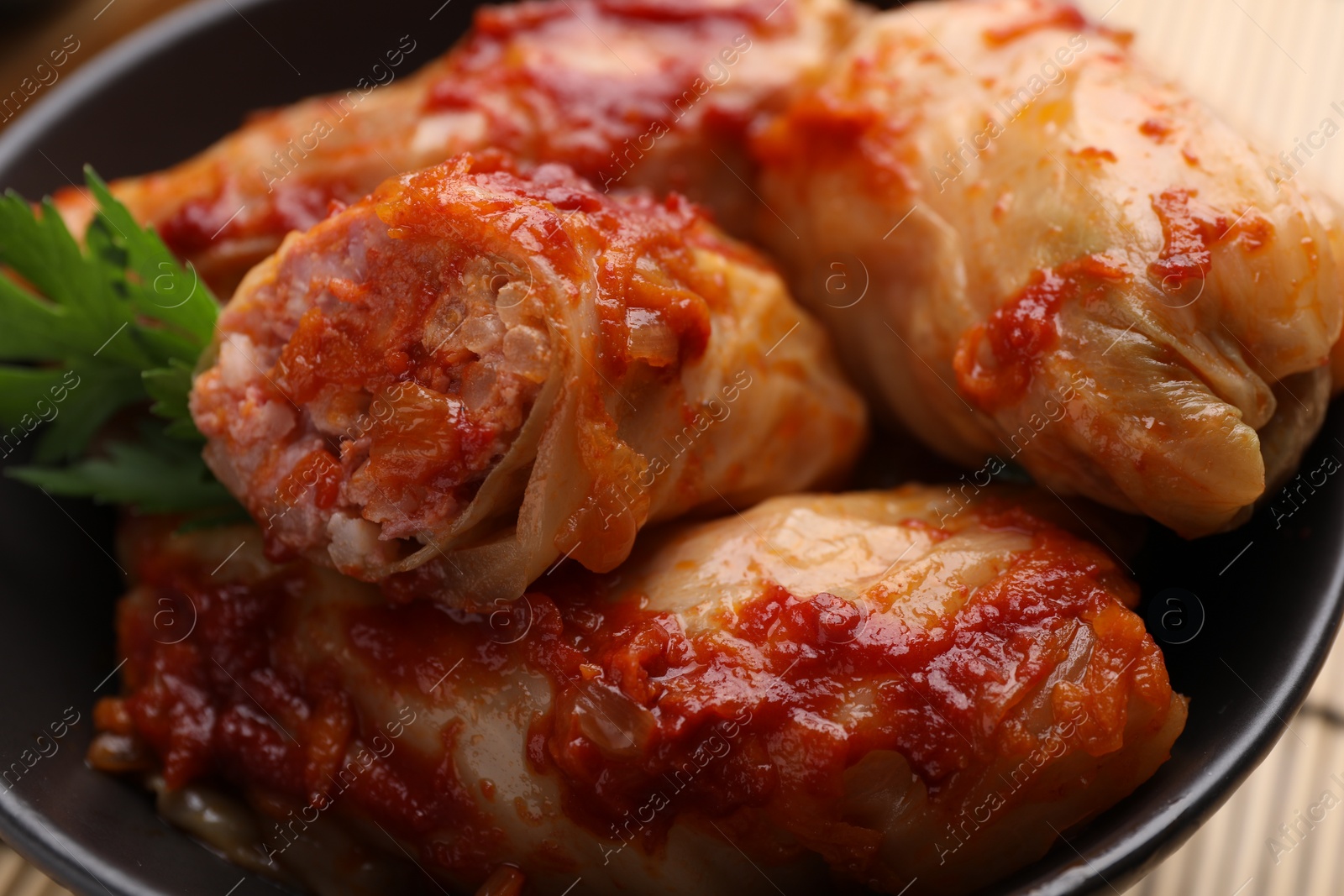 Photo of Delicious stuffed cabbage rolls cooked with homemade tomato sauce in bowl, closeup