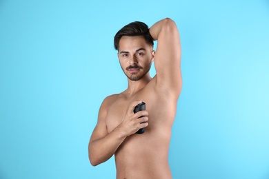 Young man using deodorant on color background