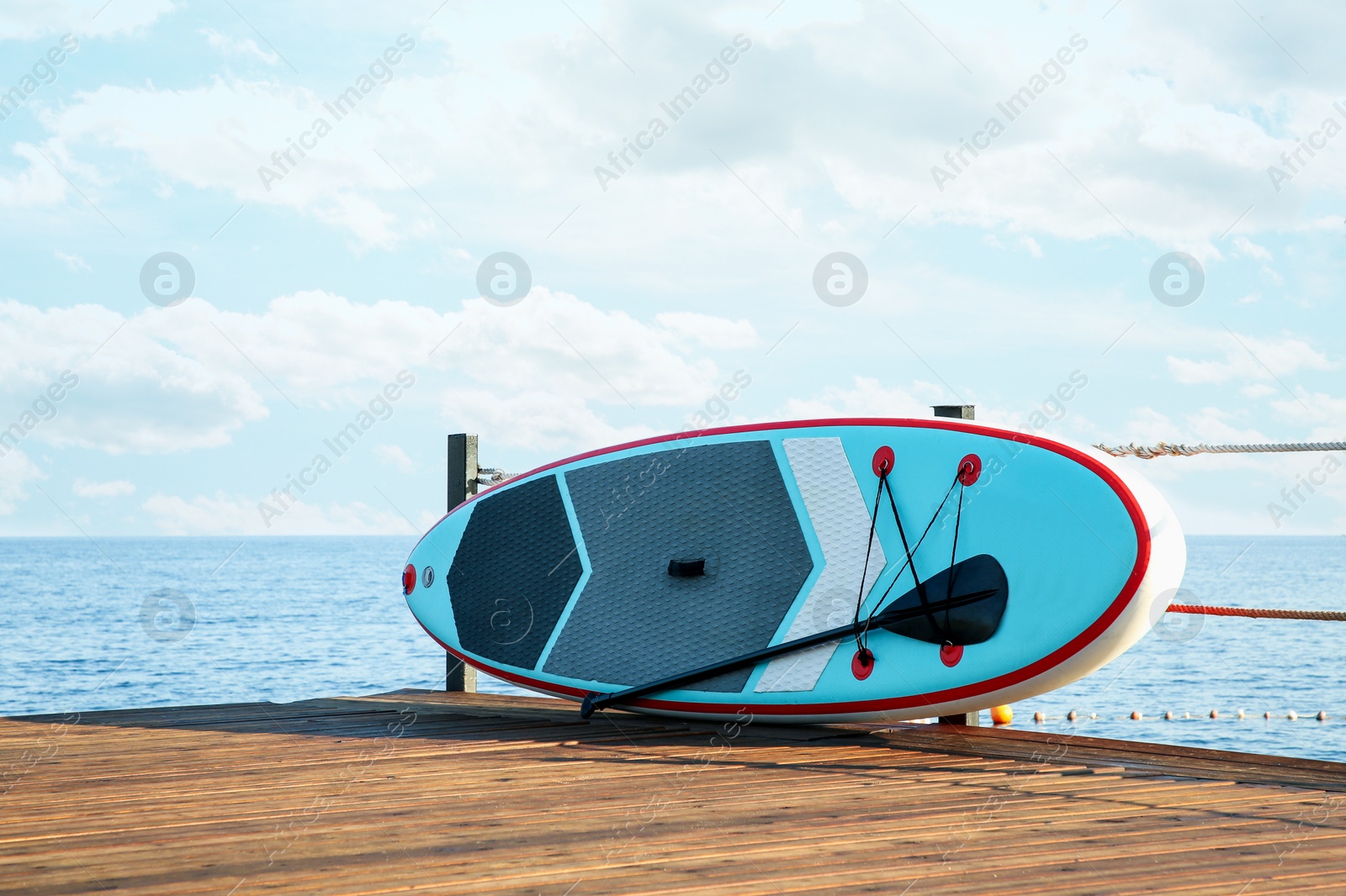 Photo of SUP board with paddle on wooden pier near sea