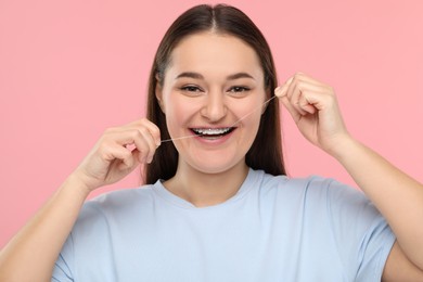 Photo of Smiling woman with braces cleaning teeth using dental floss on pink background