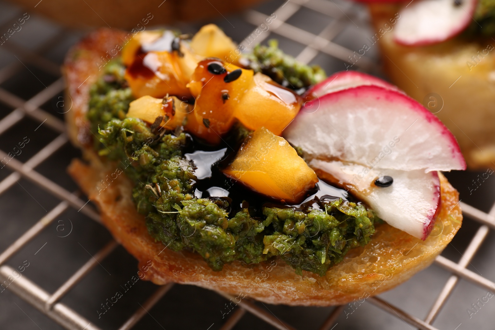 Photo of Delicious bruschetta with pesto sauce, tomatoes and balsamic vinegar on cooling rack, closeup