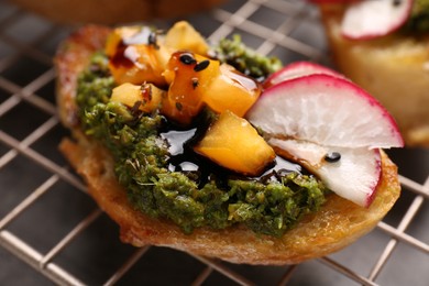 Photo of Delicious bruschetta with pesto sauce, tomatoes and balsamic vinegar on cooling rack, closeup