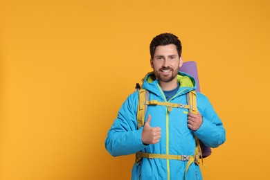 Photo of Happy man with backpack showing thumb up on orange background, space for text. Active tourism