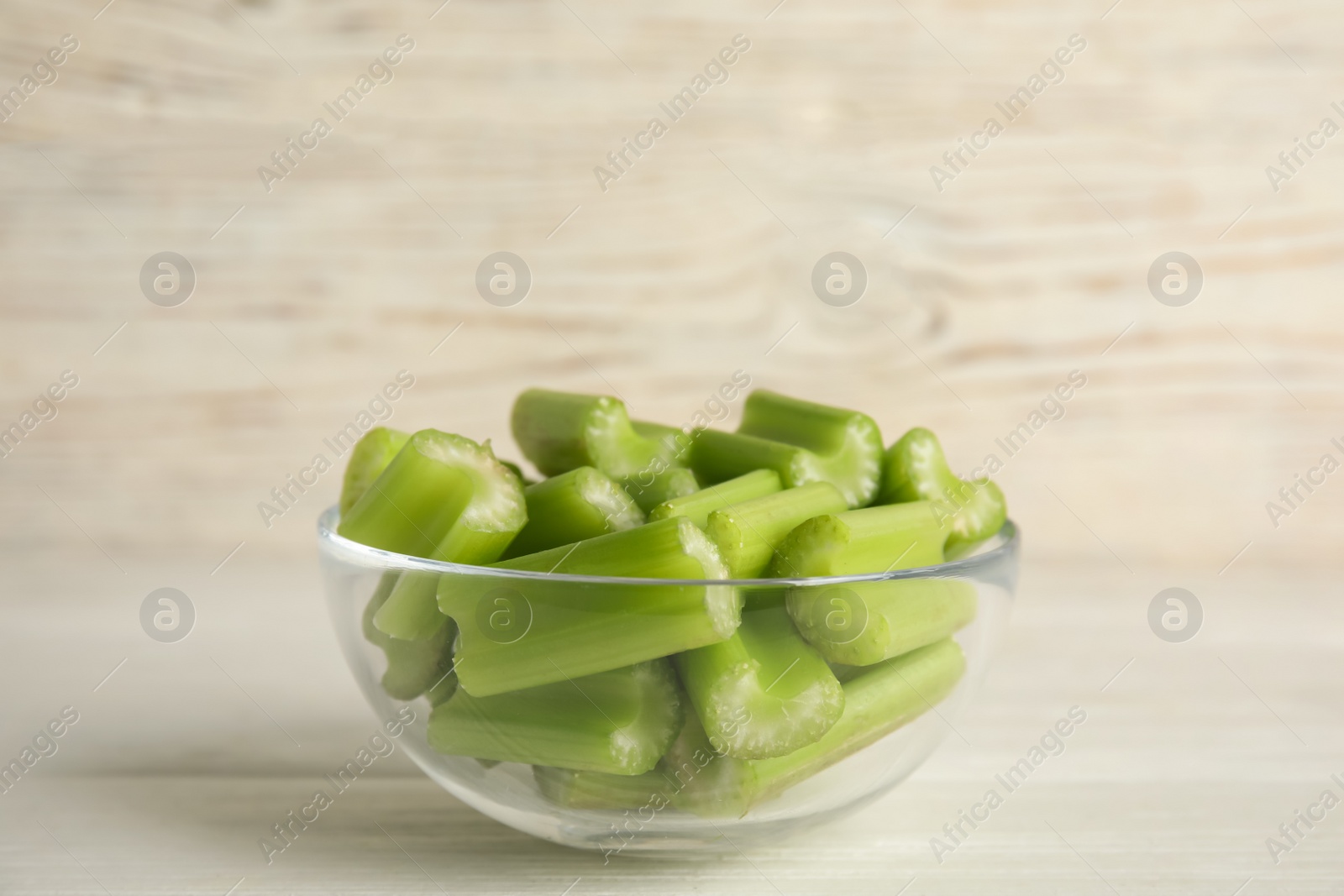 Photo of Cut celery in glass bowl on white wooden table. Space for text