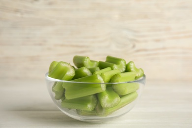 Cut celery in glass bowl on white wooden table. Space for text