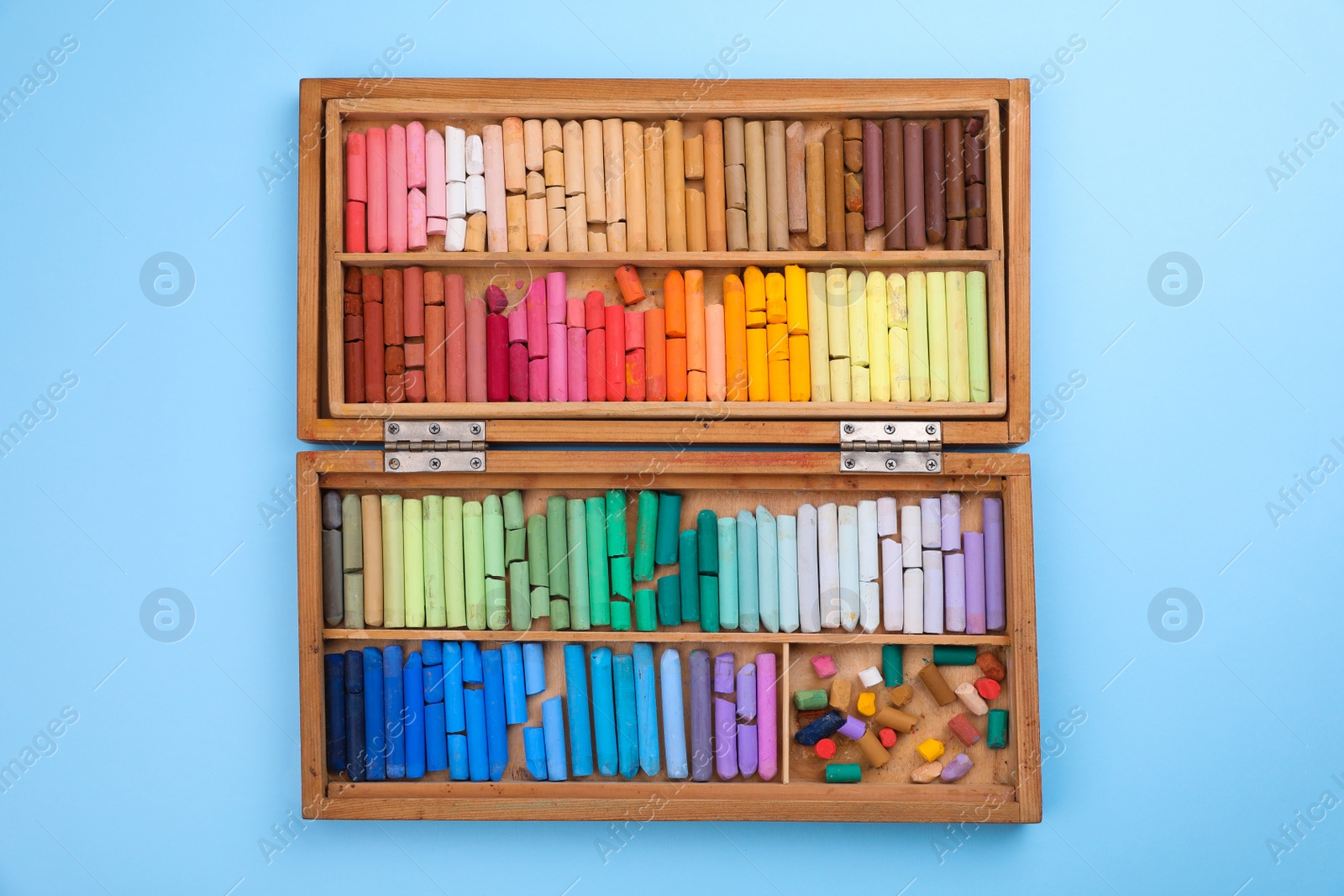 Photo of Set of soft pastels in wooden box on light blue background, top view. Drawing material