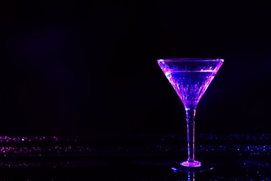 Photo of Glass of martini in neon lights on dark background. Space for text