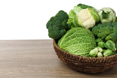 Photo of Wicker bowl with different types of fresh cabbage on wooden table against white background. Space for text