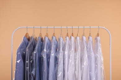 Photo of Dry-cleaning service. Many different clothes in plastic bags hanging on rack against beige background