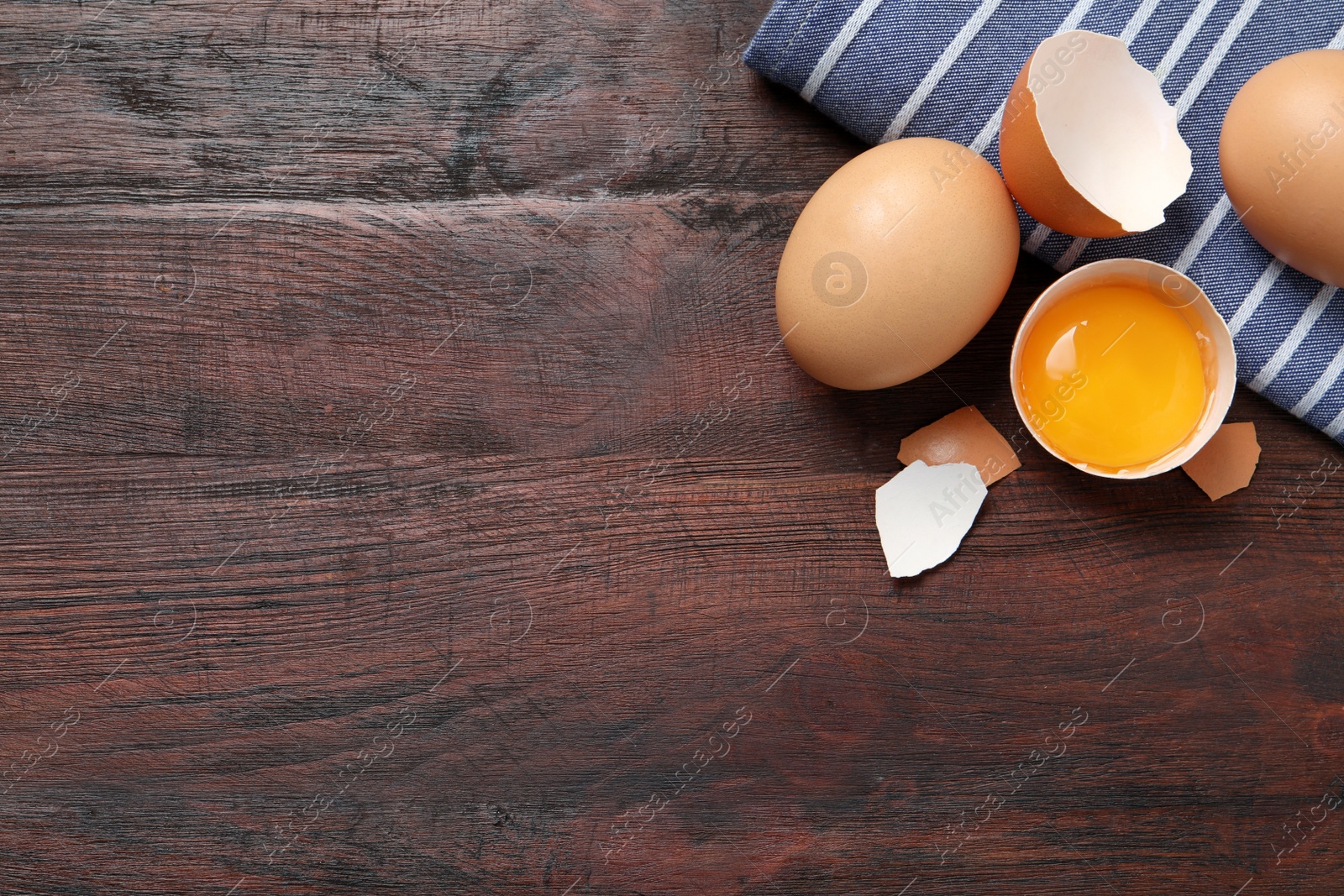 Photo of Whole and cracked chicken eggs on wooden table, flat lay. Space for text