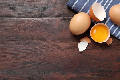 Photo of Whole and cracked chicken eggs on wooden table, flat lay. Space for text