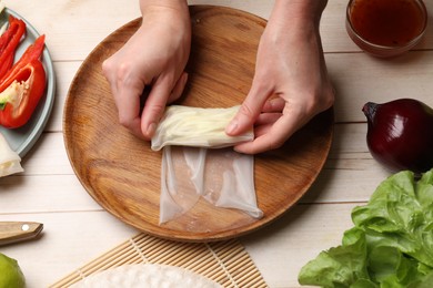 Making delicious spring rolls. Woman wrapping fresh vegetables into rice paper at wooden table, closeup