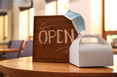 OPEN sign, packed takeout order and protective mask on table in restaurant. Food service during coronavirus quarantine