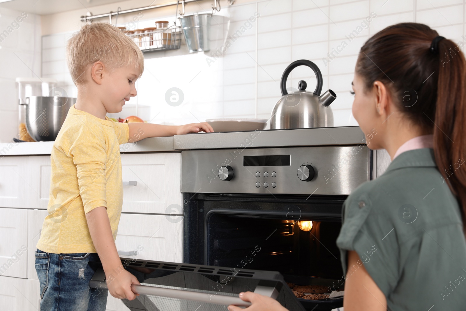 Photo of Young woman and her son baking cookies in oven at home