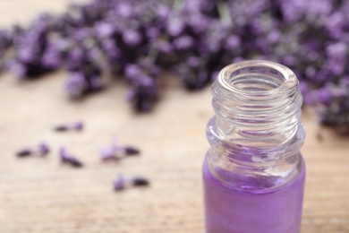 Glass bottle of natural cosmetic oil and lavender flowers on table, closeup with space for text