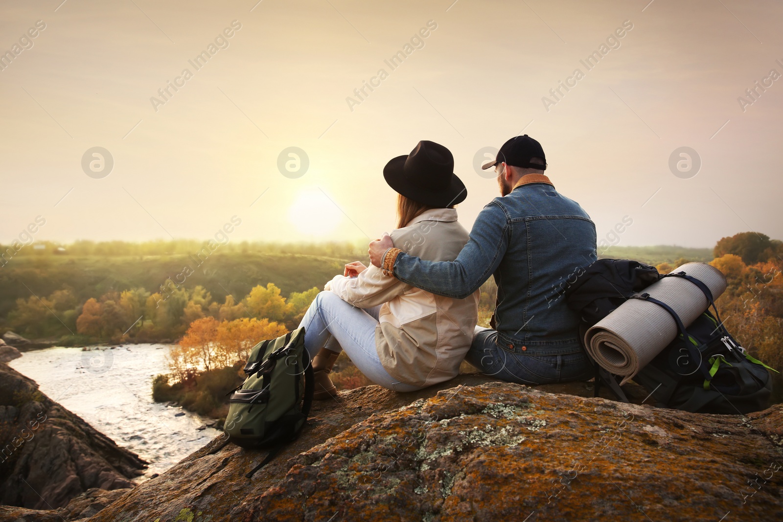 Photo of Couple of hikers with travel backpacks sitting on steep cliff