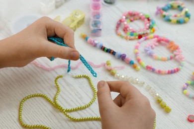 Girl making beaded jewelry at white wooden table, closeup