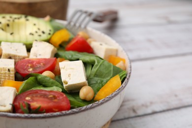 Bowl of tasty salad with tofu and vegetables on white wooden table, closeup. Space for text