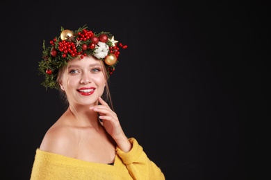 Photo of Beautiful young woman wearing Christmas wreath on black background. Space for text