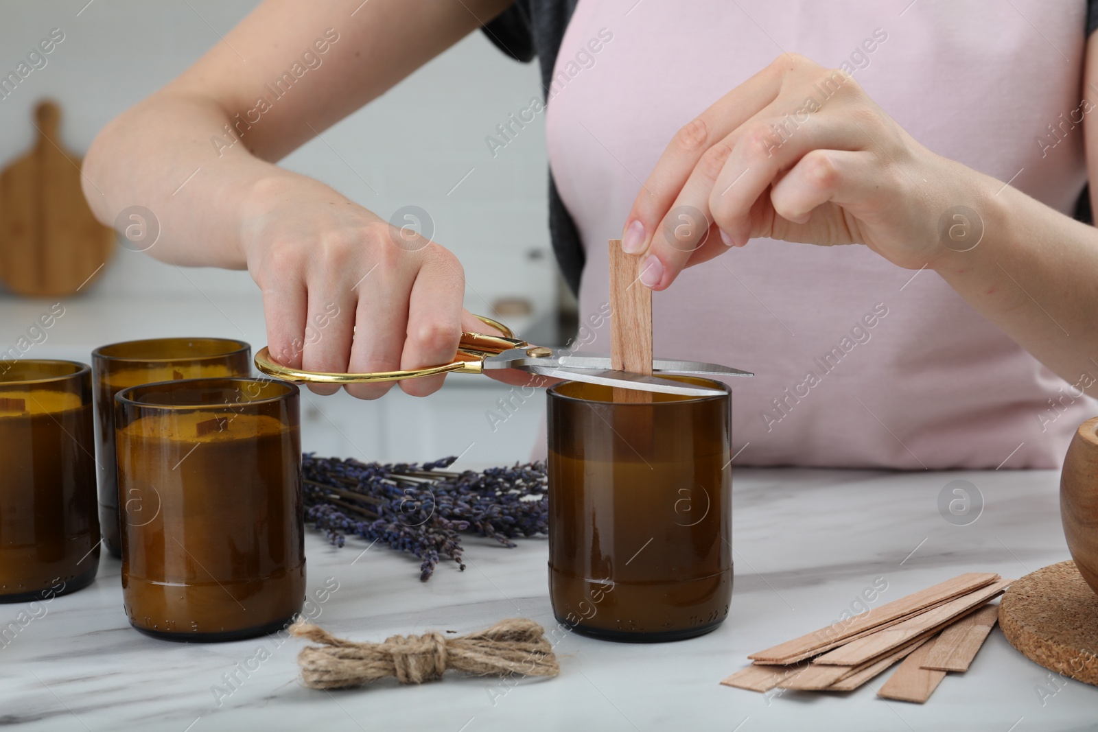 Photo of Woman cutting wick of homemade candle at table indoors, closeup