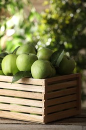 Crate full of ripe green apples and leaves on wooden table outdoors