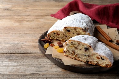 Photo of Plate of cut delicious Stollen sprinkled with powdered sugar on wooden table. space for text